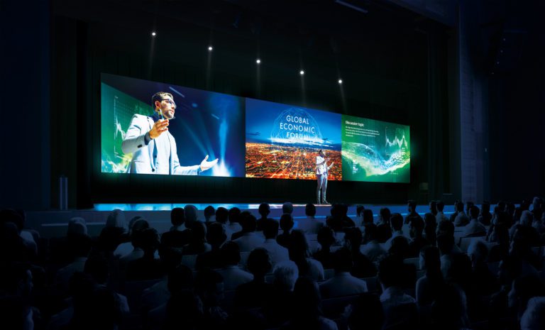 Business Forum Economics Conference Stage: Visionary Female Chief Analyst Delivers Speech and Shows Infographics, Statistics on Movie Theater Screen. Presentation with Speaker in Full Auditorium Hall